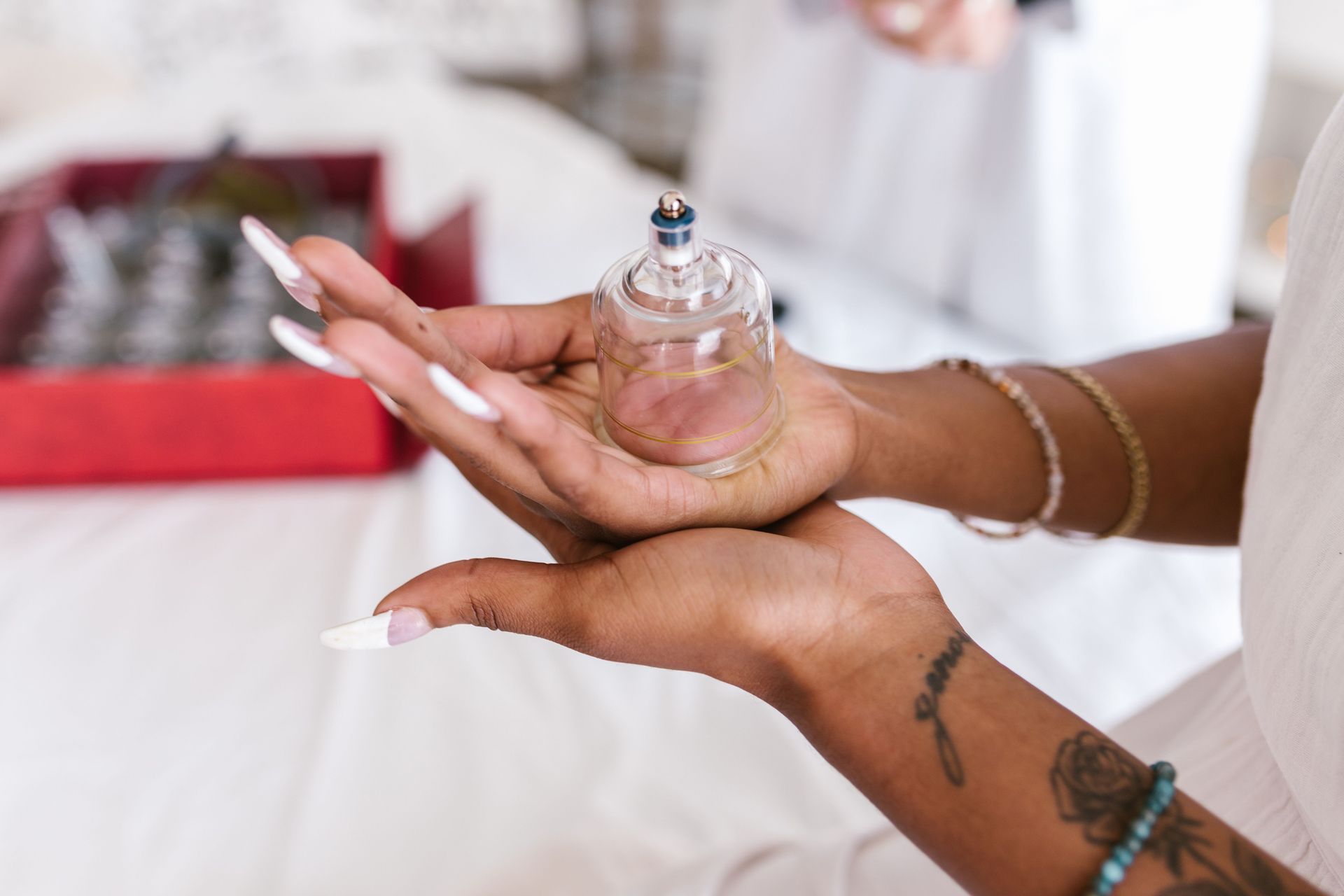 A close-up view of hands holding a cupping therapy cup, showcasing detailed manicure and tattoos.